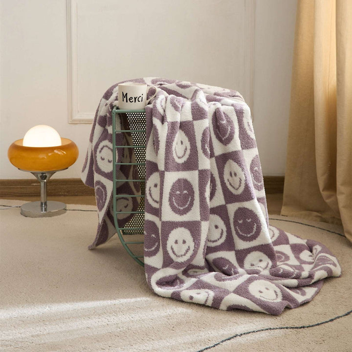 itsdecorszn fluffy purple and white checkerboard blanket with smiling face patterns draped over a wire basket