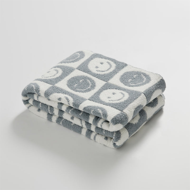 itsdecorszn grey and white knitted checkerboard blanket with smiling face patterns, folded on a white background.