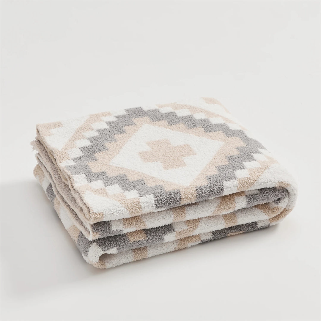 Geometric quilt blanket folded, with beige, cream, and gray diamond motifs