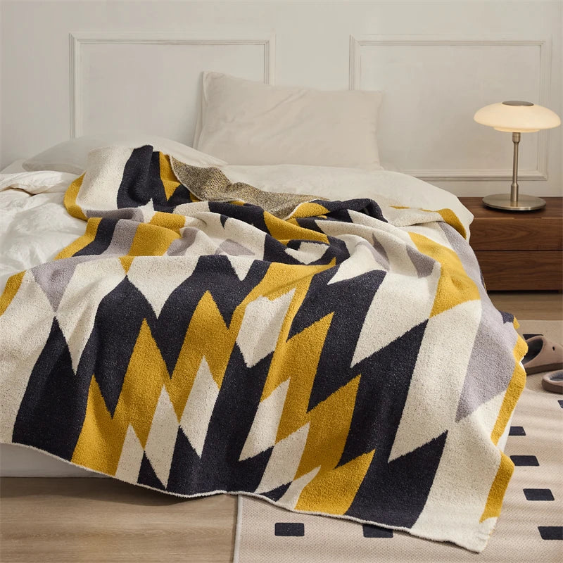 Yellow, charcoal, gray and cream geometric zigzag blanket draped across a bed.