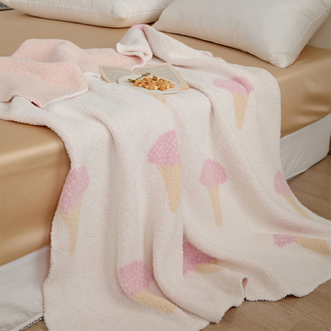 Ice cream pattern blanket draped over a bed, with a soft cream pile and pink cone motifs