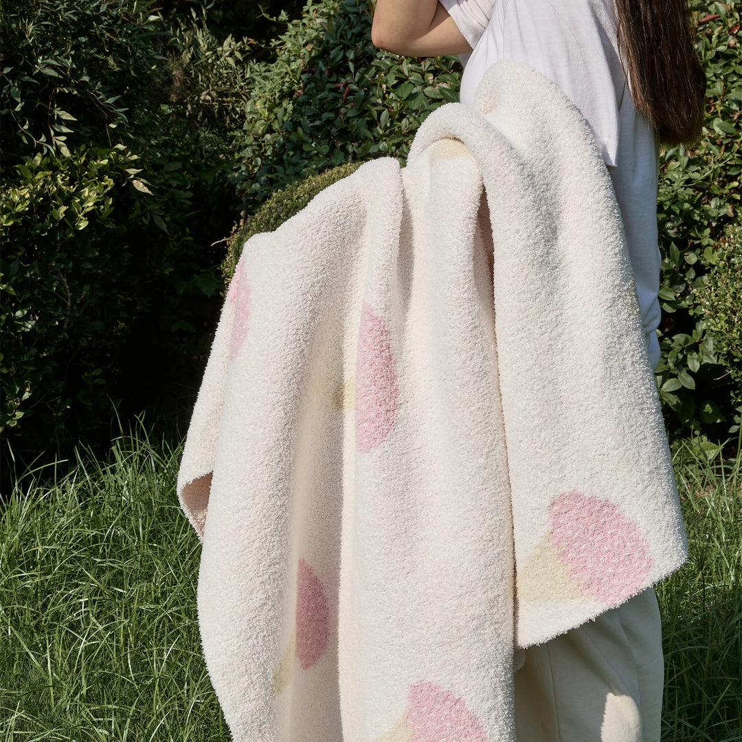 Ice cream pattern blanket held up, with a cream plush surface and scattered pink cone motifs