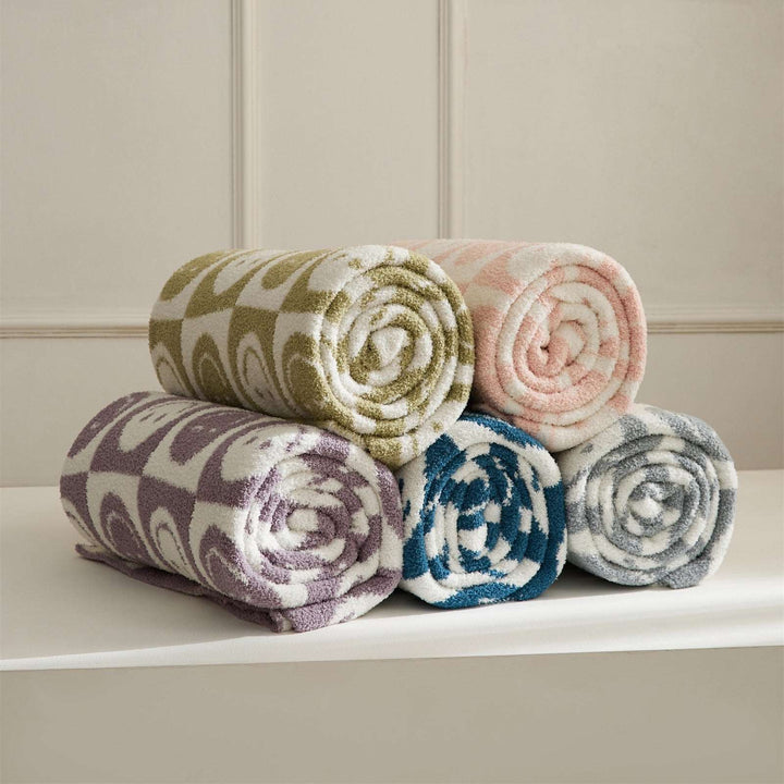 itsdecorszn fluffy knitted checkerboard blankets in five assorted pastel and vibrant colors rolled in a stack.