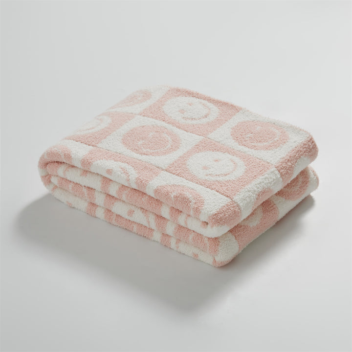 itsdecorszn pink and white checkerboard knitted blanket with smiling face pattern, folded on a white background.