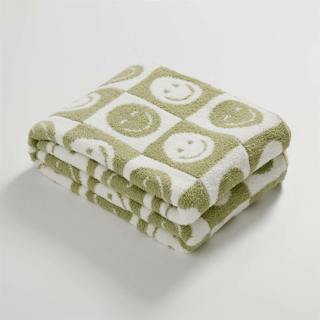 itsdecorszn fluffy knitted checkerboard blanket in sage green and white with smiling face patterns.