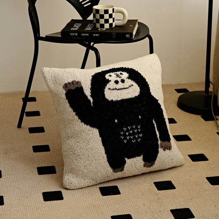 Kawaii Gorilla pillow with a waving black gorilla on a cream background, resting on a patterned rug