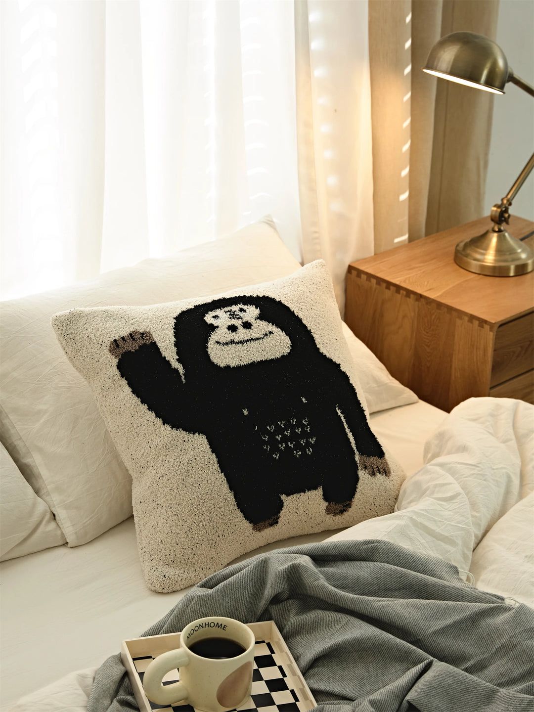 Waving black gorilla Kawaii Gorilla pillow styled on white bedding beside a wooden nightstand