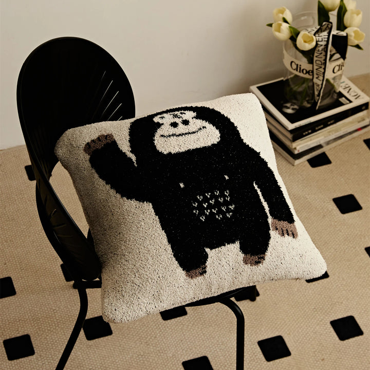Angled view of a cream Kawaii Gorilla pillow with a waving black gorilla on a black chair