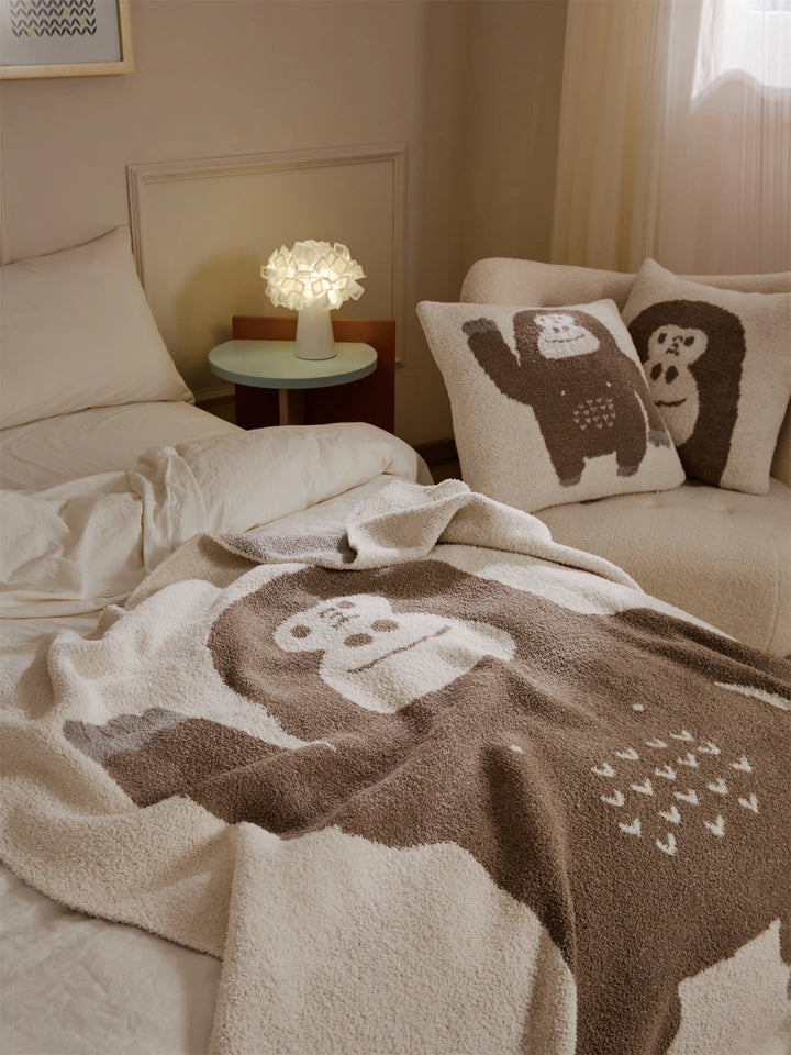 Brown gorilla throw blanket spread across a bed, with a cream cartoon gorilla design