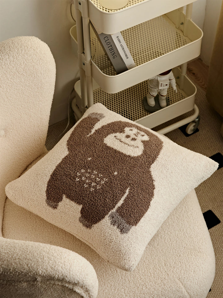 Overhead view of a waving brown gorilla Kawaii Gorilla pillow on a cream chair