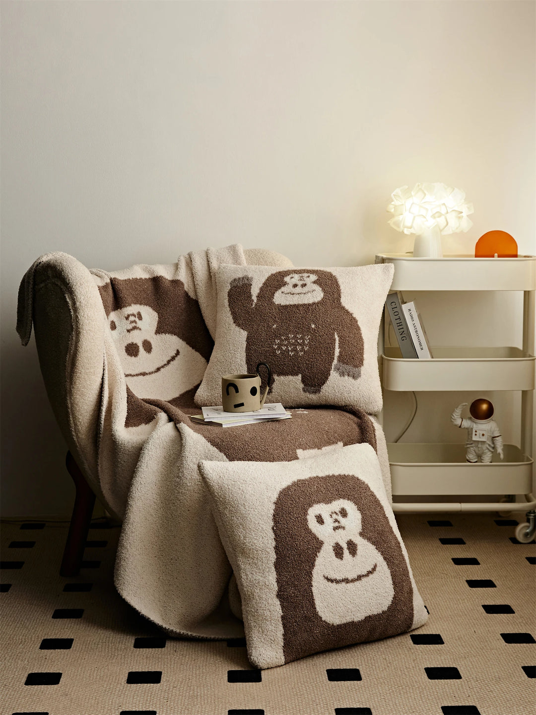 Brown Kawaii Gorilla throw blanket and matching waving-gorilla and gorilla-face pillows styled on and beside a cream chair