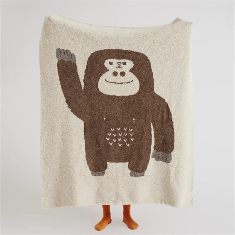 Cream throw blanket with a large brown cartoon gorilla and small heart details