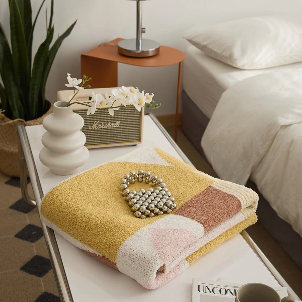 Folded Kawaii Tangram blanket showing a textured surface and mustard, brown, pink and cream shapes.