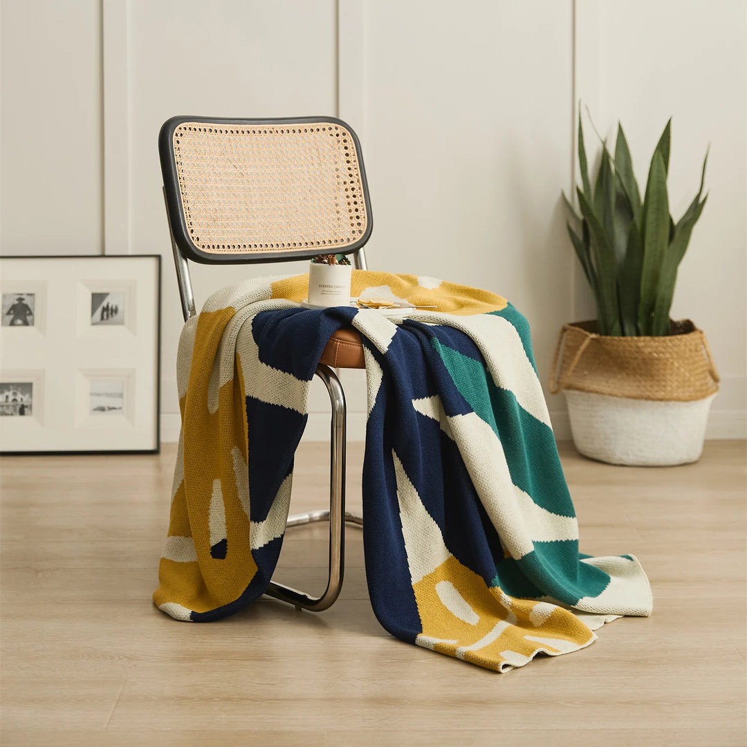 Leaf jacquard blanket spread over a chair with bold navy, teal, and mustard shapes