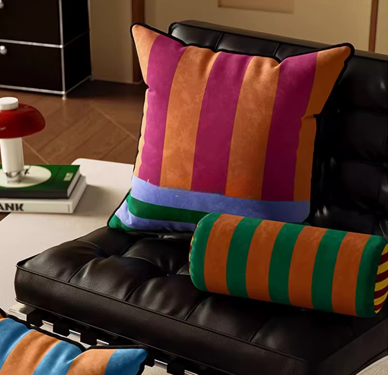 Square retro pillow with orange and pink stripes and a blue-green border, beside a matching bolster