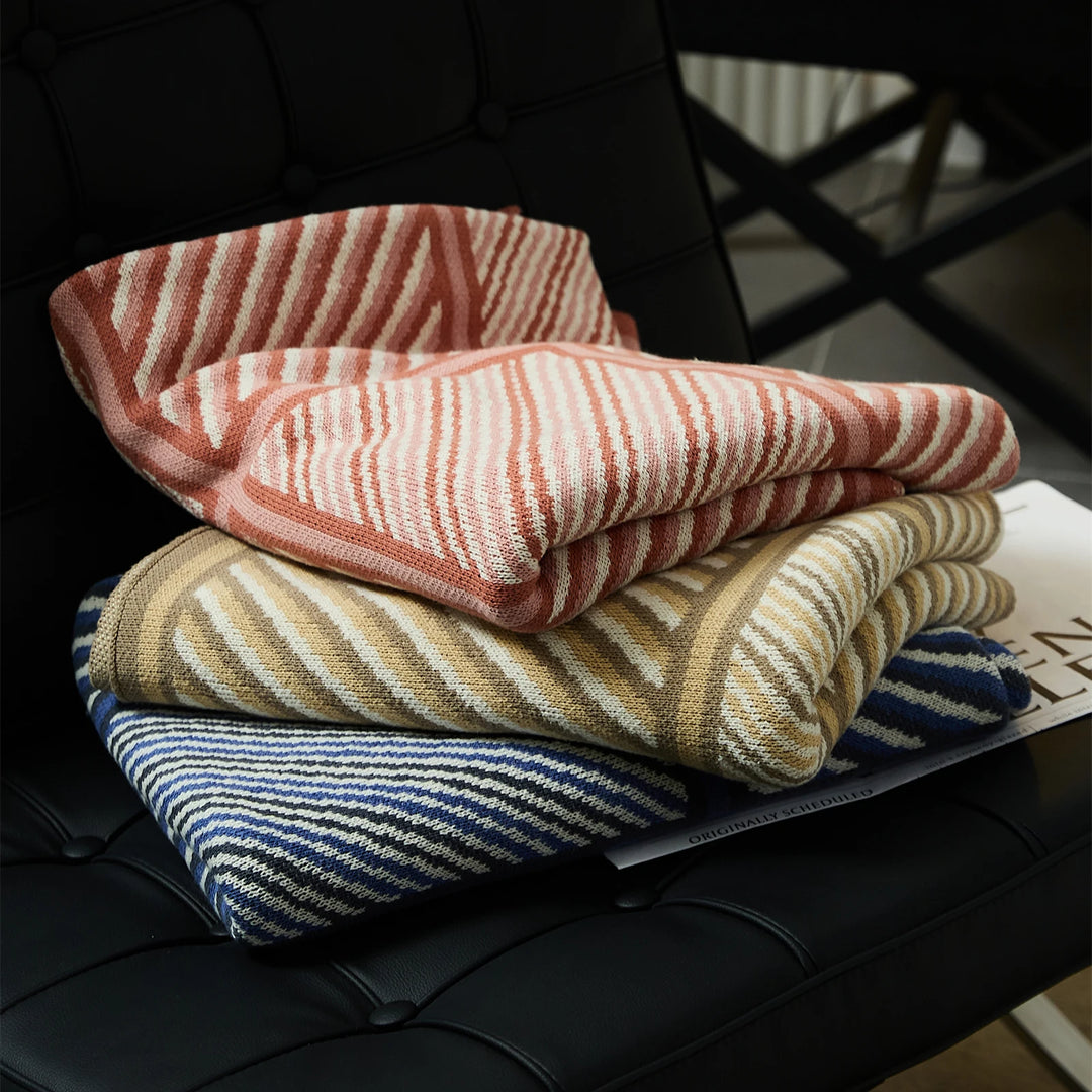 Striped blankets in pink, beige, and blue, folded to show their woven patterns