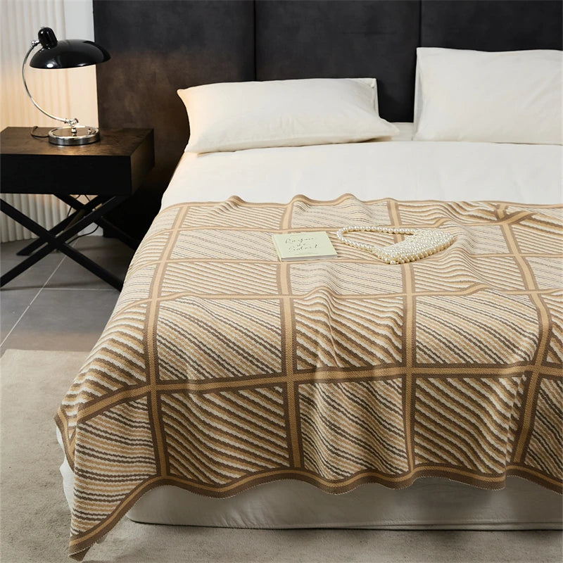Beige and cream blanket with large plaid squares and diagonal stripes spread on a bed.