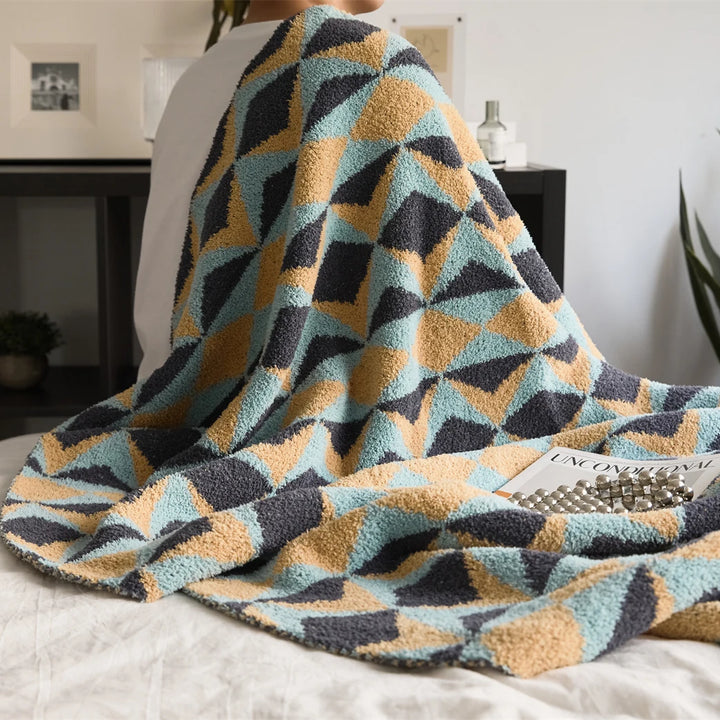Plush geometric blanket draped over a person, showing blue, mustard, and charcoal triangles.