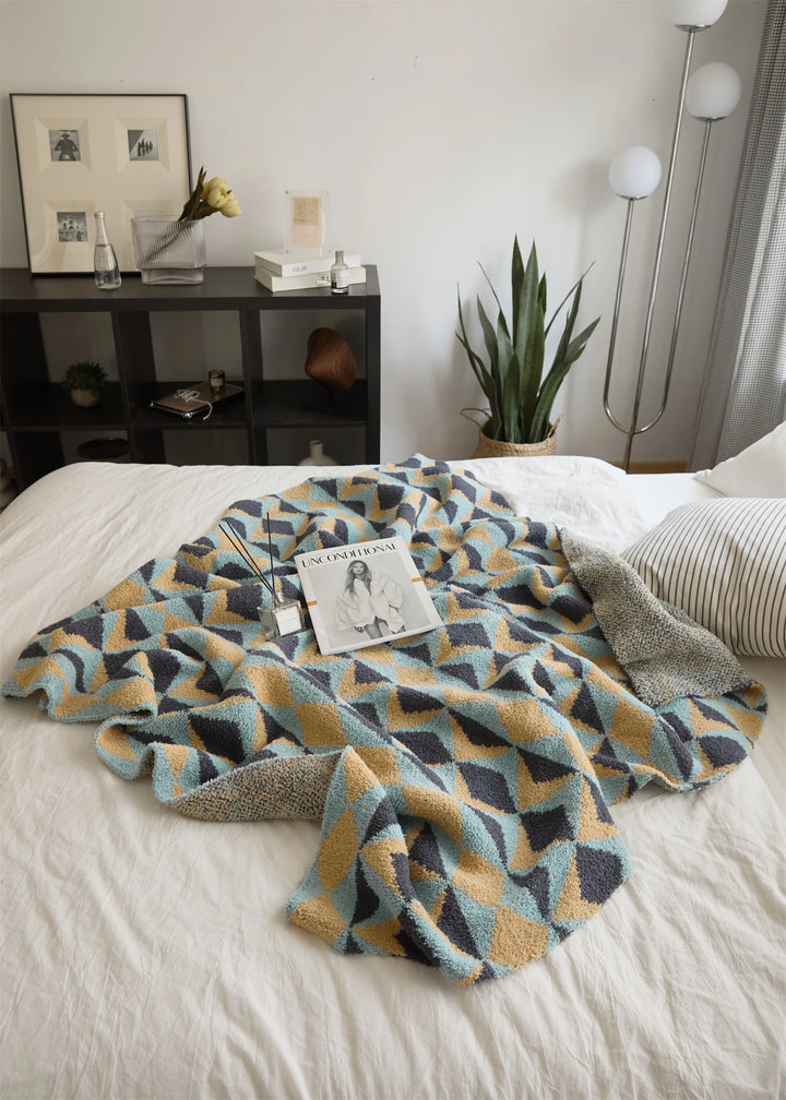 Geometric blanket loosely folded on a bed, revealing its patterned face and woven reverse.