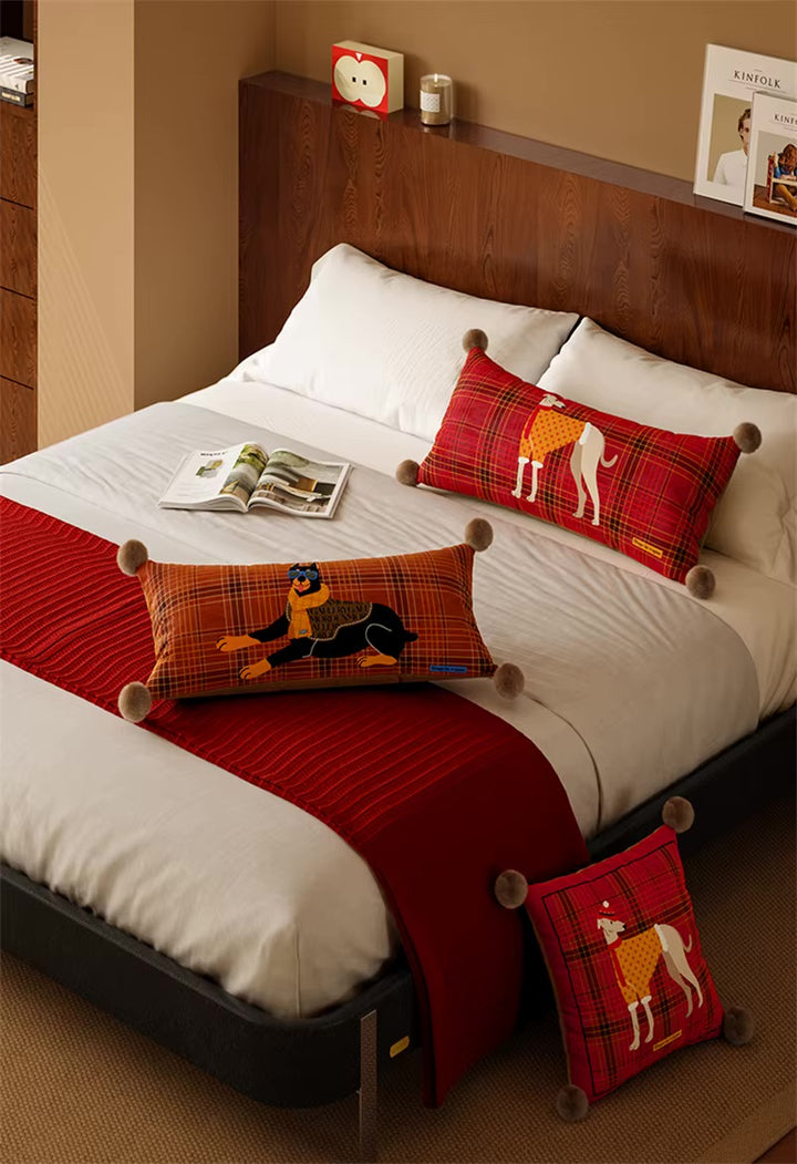 Red and rust plaid dog pillows with greyhound and Doberman prints, shown on a bed