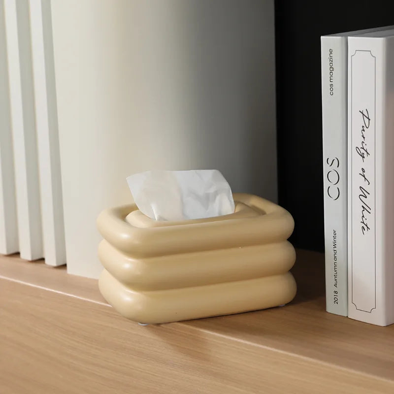 Creamy yellow square tissue holder with rounded stacked sides and a tissue through the top.