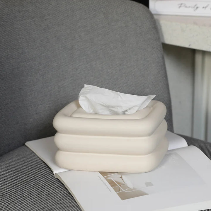 White square tissue holder with rounded stacked sides and a tissue pulled through the top.
