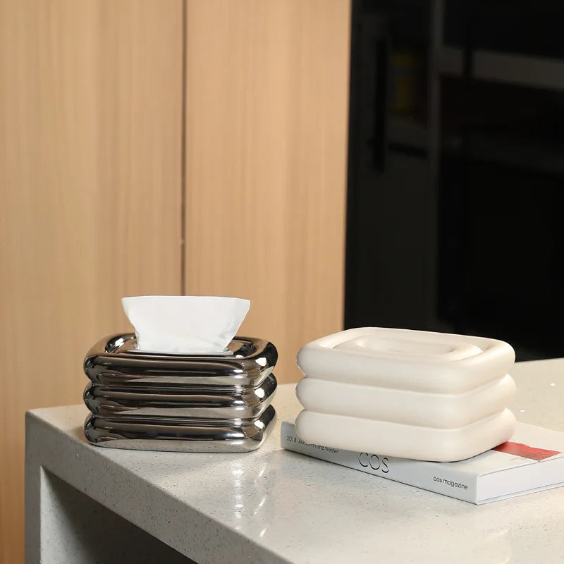 Silver and white square tissue holders with rounded stacked sides; a tissue protrudes from the silver one.