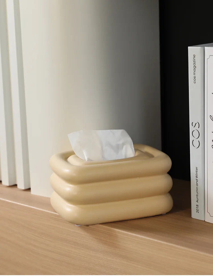 Creamy yellow square tissue holder with rounded stacked sides and a tissue through the top.