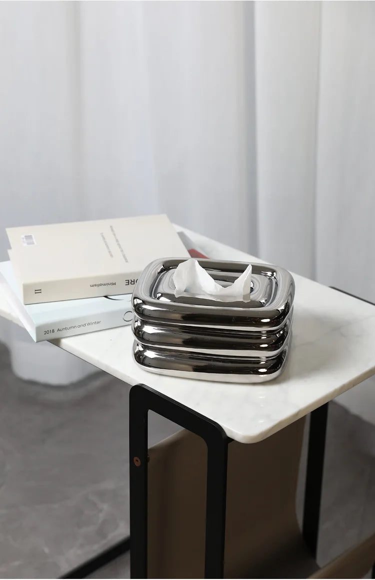 Silver square tissue holder with rounded stacked sides and a tissue pulled through the top.