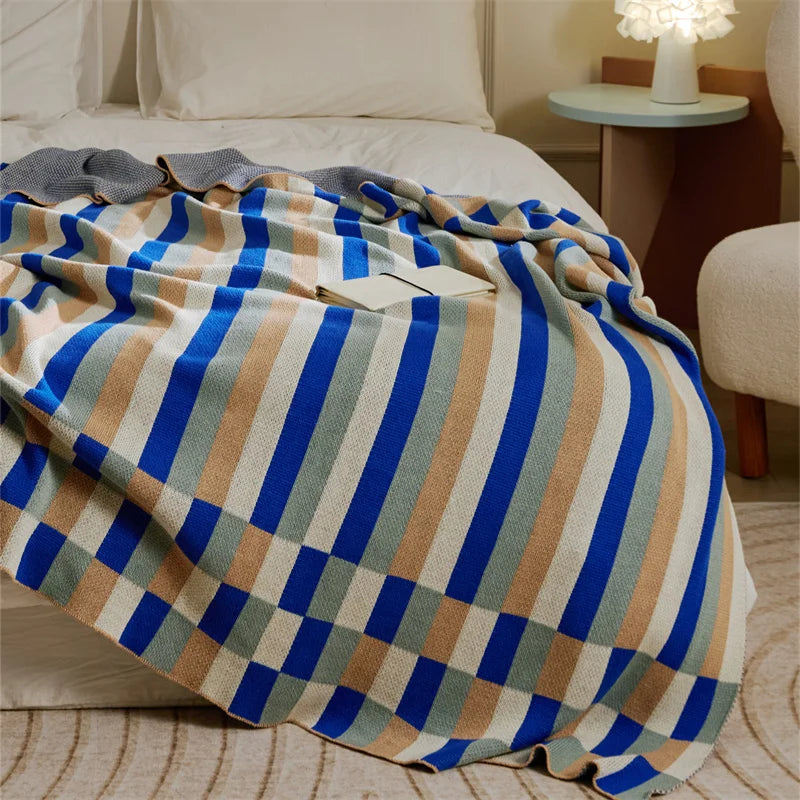 Blue, beige, gray and cream striped knitted blanket draped across a bed.
