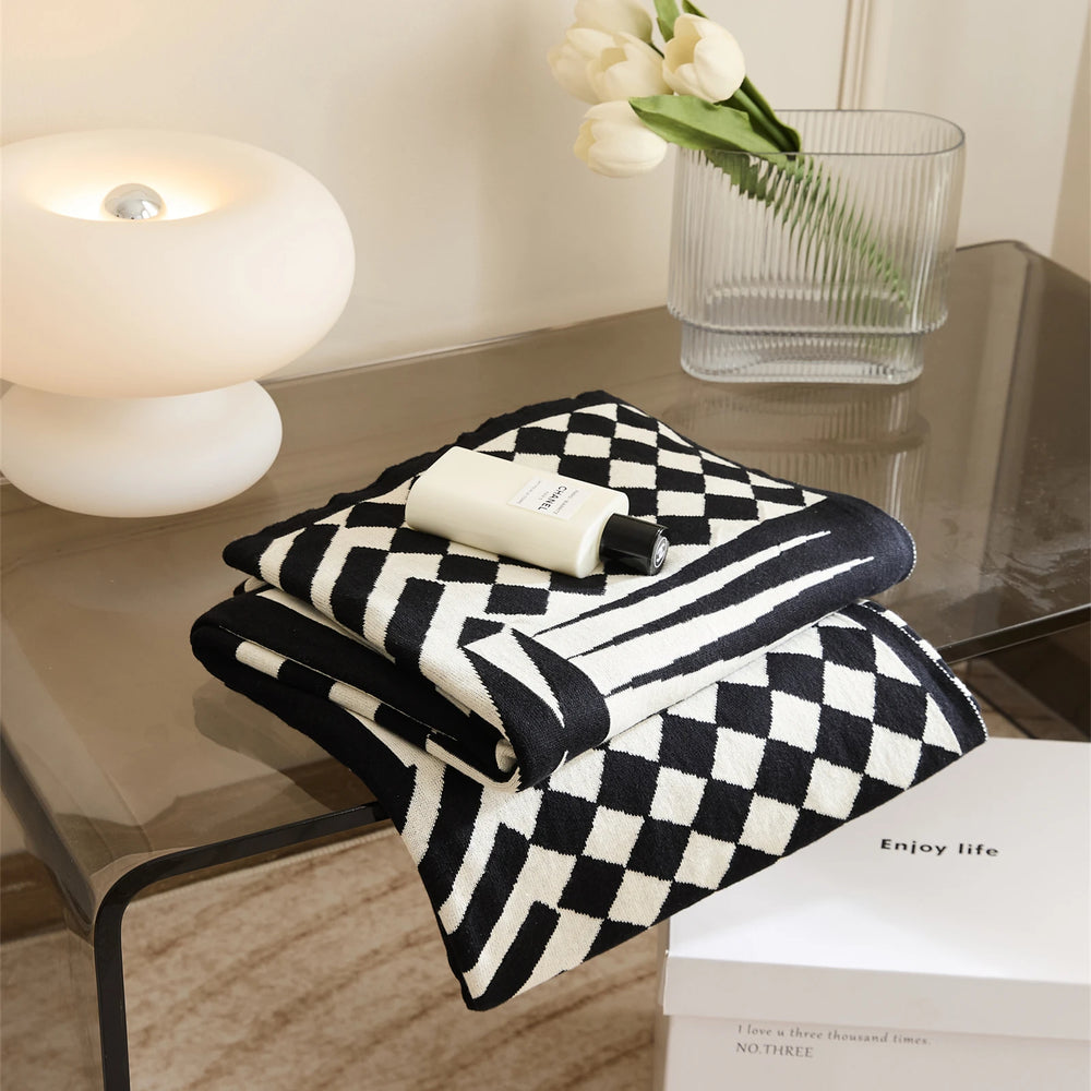 Folded black and cream geometric blanket with a checkerboard pattern and striped border.