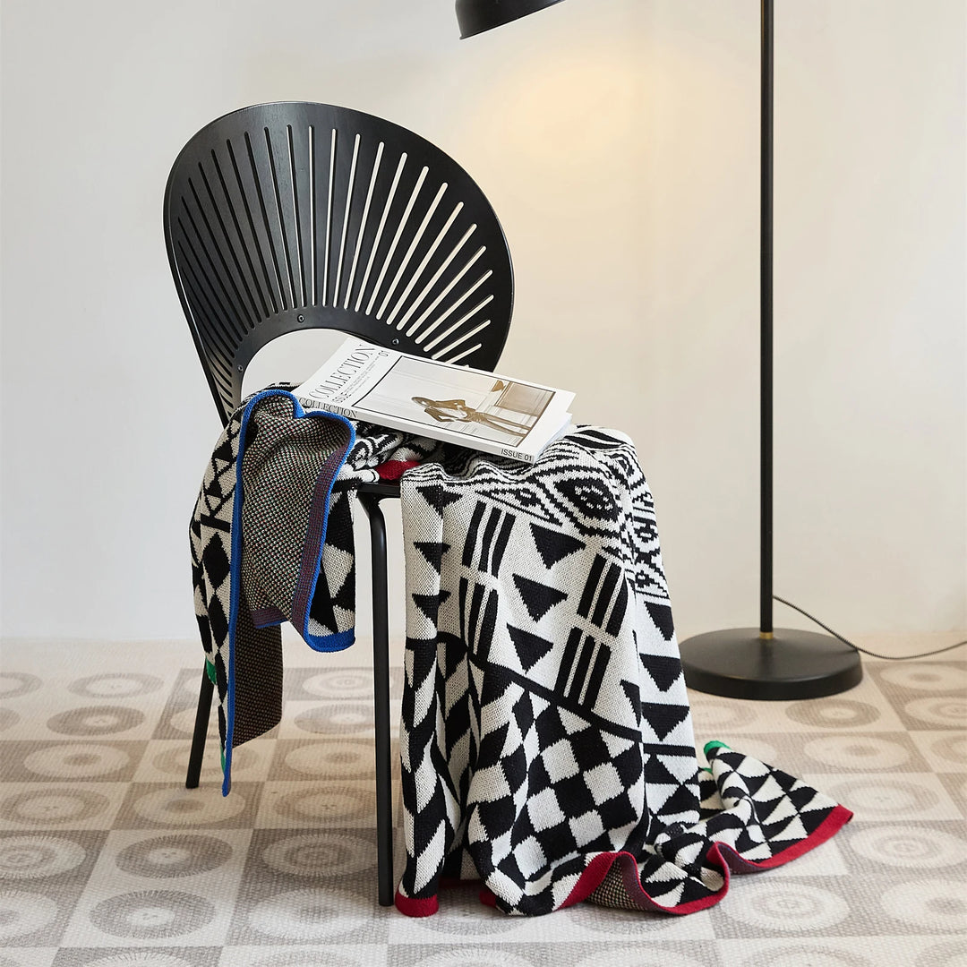 Black and ivory geometric blanket with red, blue, and green edge trim draped over a chair
