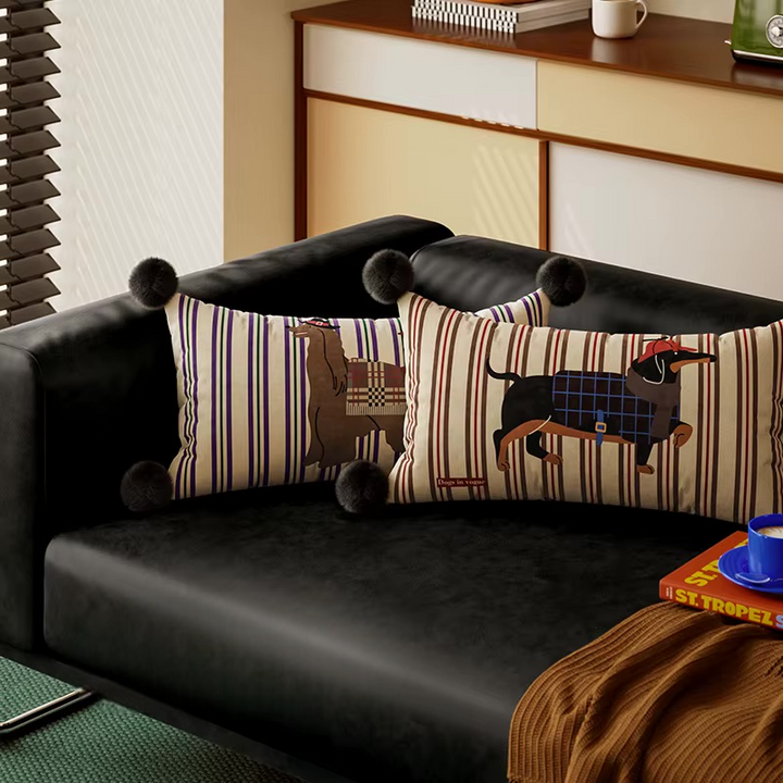 Two striped dog-print lumbar pillows with black pom-pom corners on a sofa