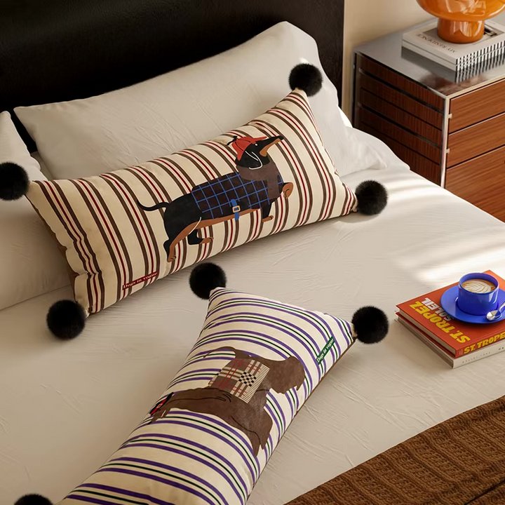 Two striped dog-print lumbar pillows with black pom-pom corners on a bed