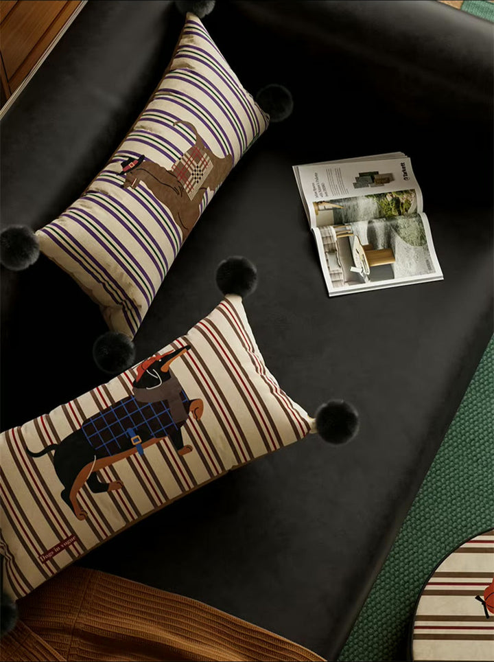 Two striped dog-print lumbar pillows with black pom-pom corners on a sofa