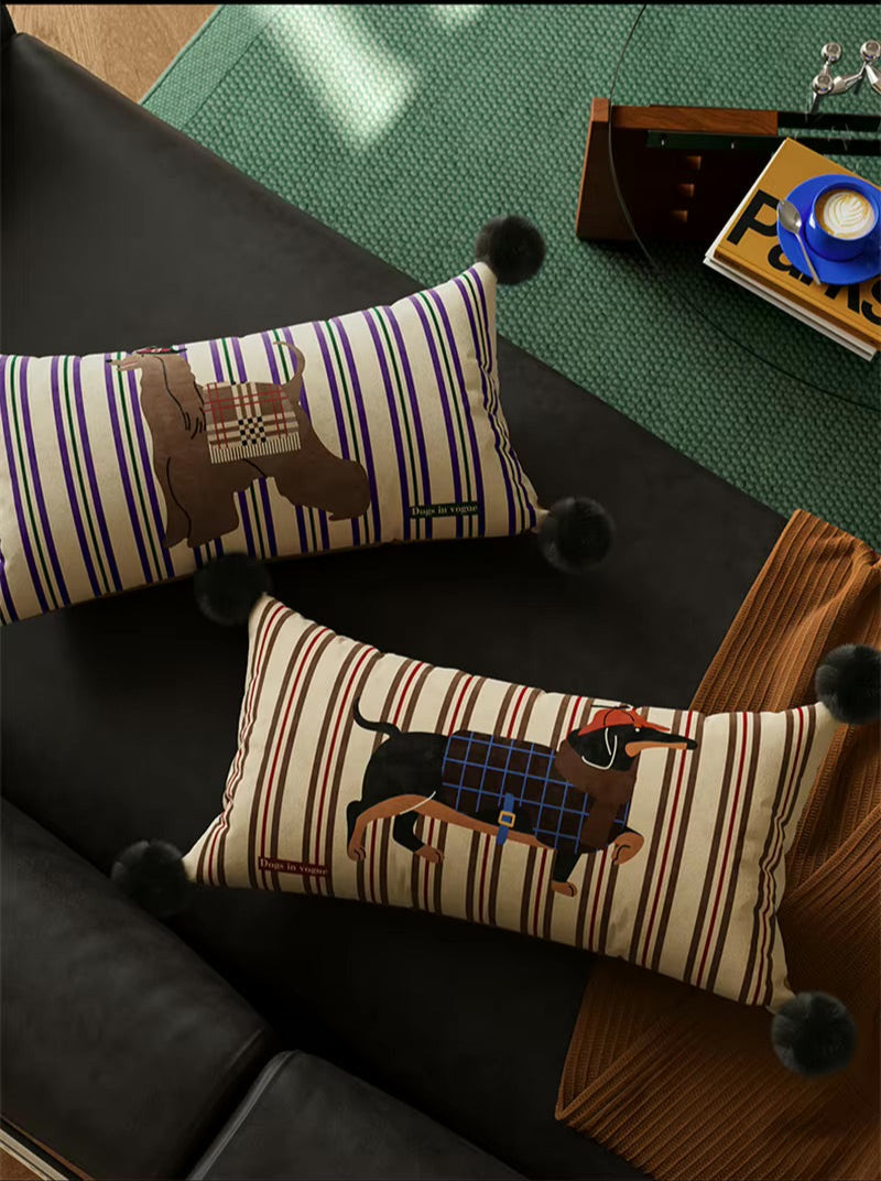Two striped dog-print lumbar pillows with black pom-pom corners on a sofa