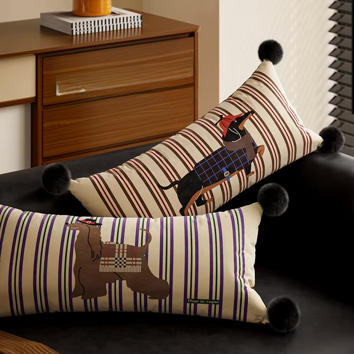 Two striped dog-print lumbar pillows with black pom-pom corners on a sofa