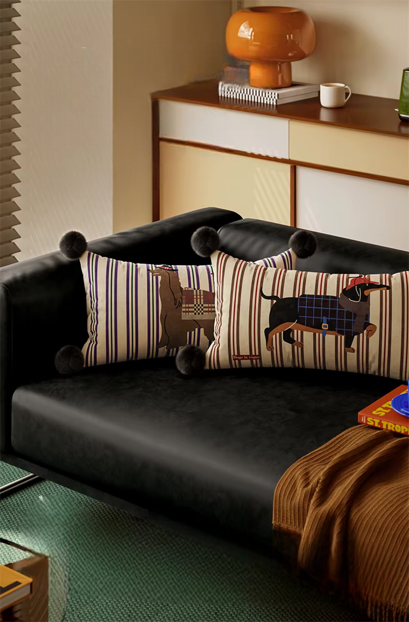 Two striped dog-print lumbar pillows with black pom-pom corners on a sofa