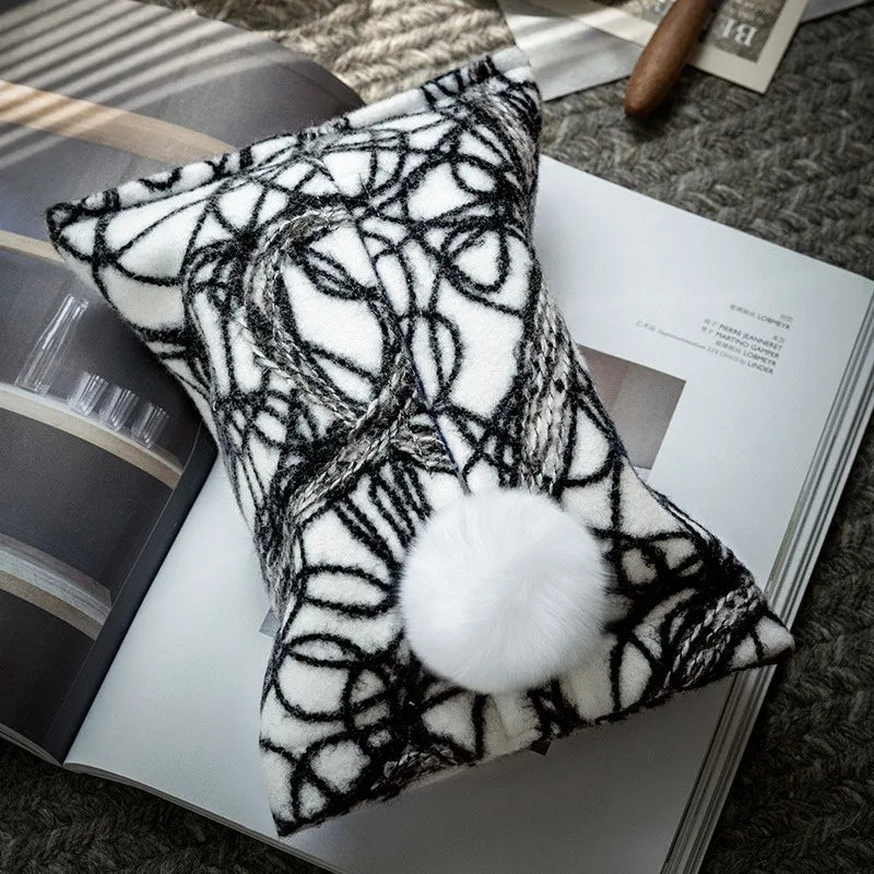 White woven tissue holder with black looping pattern and white pom-pom