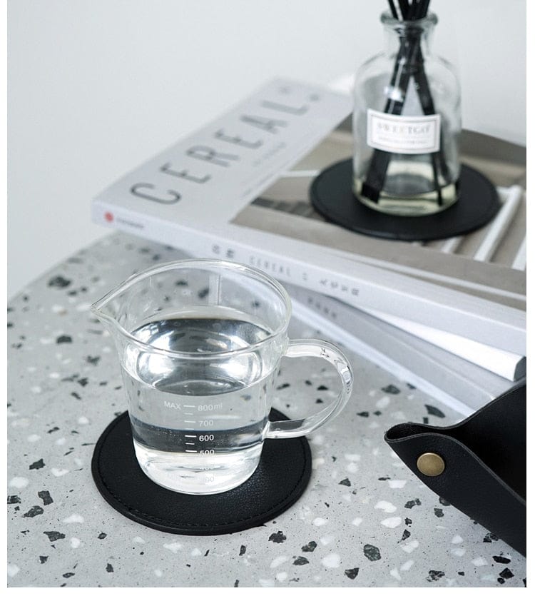A black leather coaster set and a transparent glass cup.