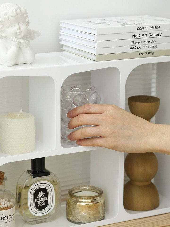 Acrylic storage holder with white finish having some products organized and a person keeping a glass cup on a shelve. 