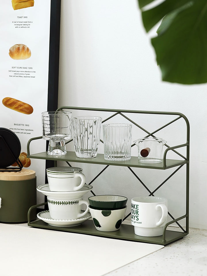 Green metal shelf with some glass cups and mugs organized on two levels.