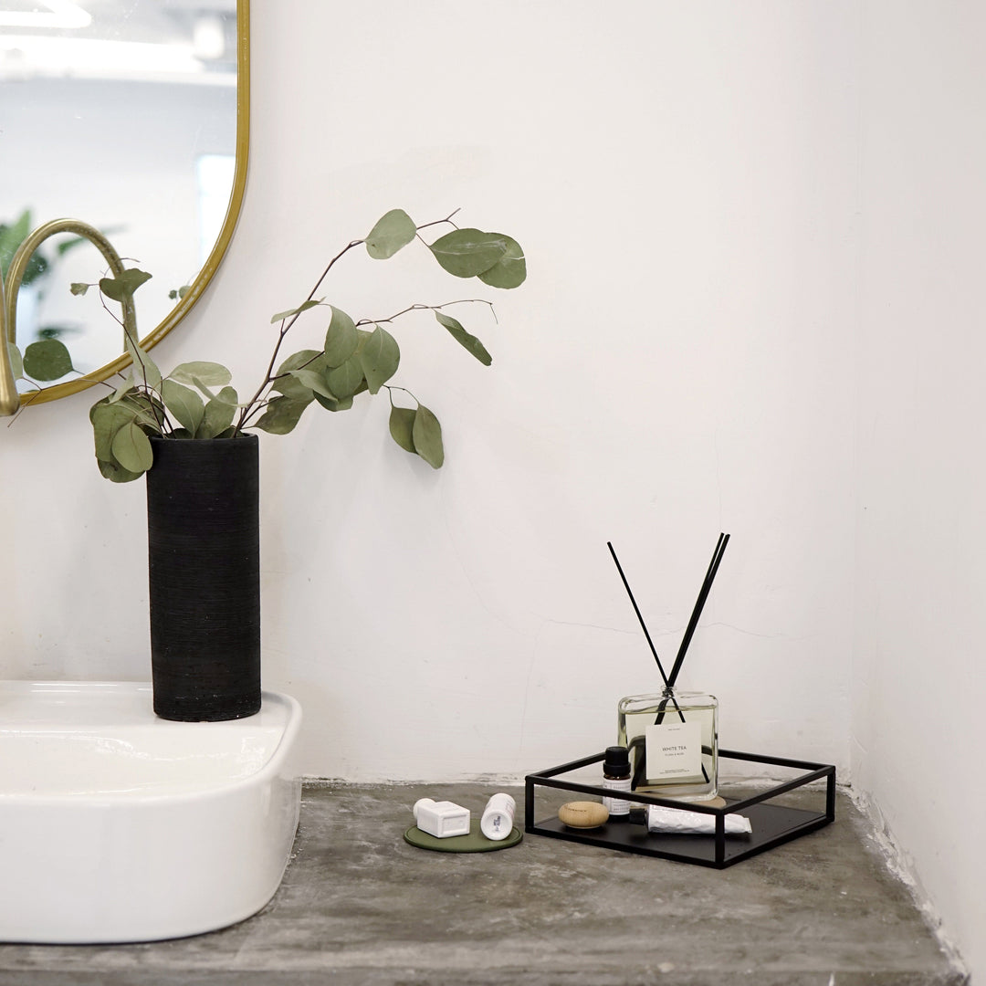 A metal decoration tray in black with some beauty products placed and a beautiful black flowerpot left on it.
